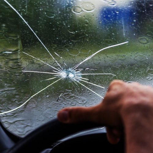 Broken windshield of a car. A web of radial splits, cracks on the triplex windshield. Broken car windshield, damaged glass with traces of oncoming stone on road or from bullet trace in car glass