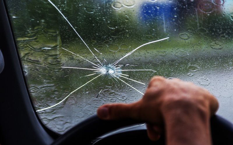 Broken windshield of a car. A web of radial splits, cracks on the triplex windshield. Broken car windshield, damaged glass with traces of oncoming stone on road or from bullet trace in car glass